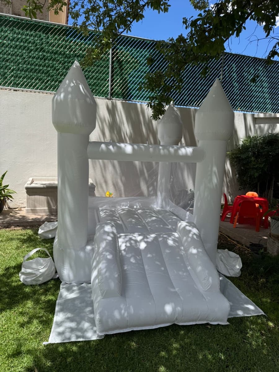 Castillo inflable blanco al aire libre en jardín con árbol y sillas rojas